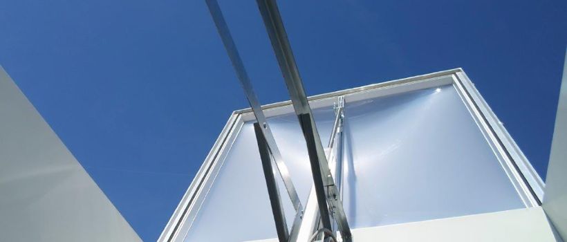 Eine Lichtkuppel, bestehend aus Zarge, Kuppel und Öffnungssvorrichtung, auf einem Flachdach montiert. Die Öffnungsvorrichtung, hier pneumatisch, ermöglicht Öffnungswinkel von 140° für eine optimale RWA-Entrauchung.